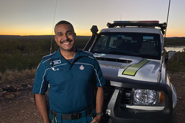 A man in a blue shirt stands beside a white truck, smiling and looking towards the camera.