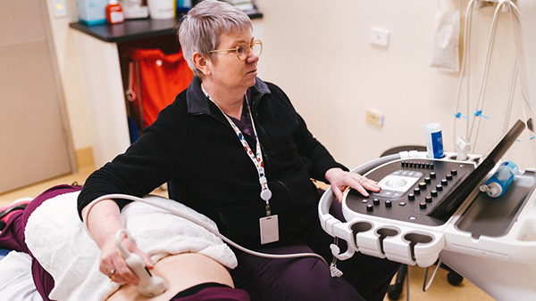 A woman operates an ultrasound machine while examining a patient in a clinical setting.