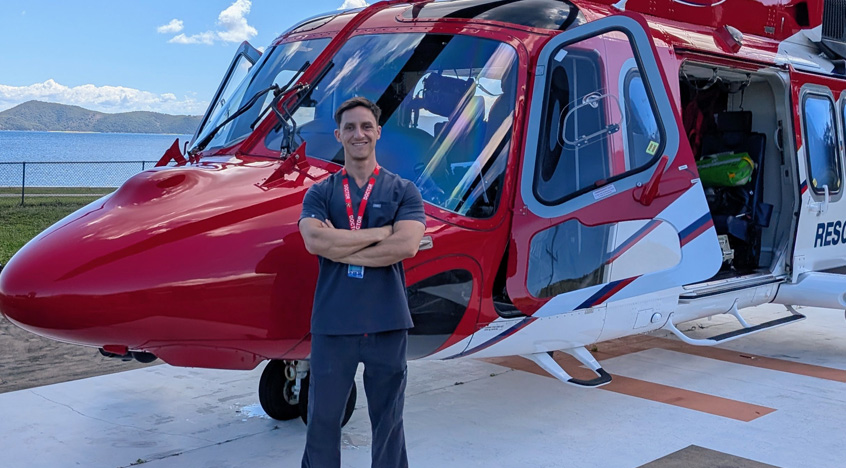 A man stands in front of a red and white helicopter, showcasing the aircraft's vibrant colors and design.