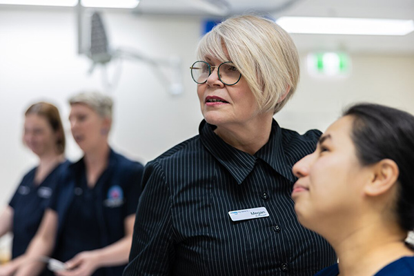 A audiologist wearing glasses talks with another audiologist in a medical setting, both appearing engaged in discussion.