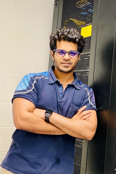 A man wearing a blue shirt and glasses stands in front of a server rack.