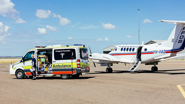 A small RFDS plane parked on the ground next to an ambulance, ready for medical emergencies.