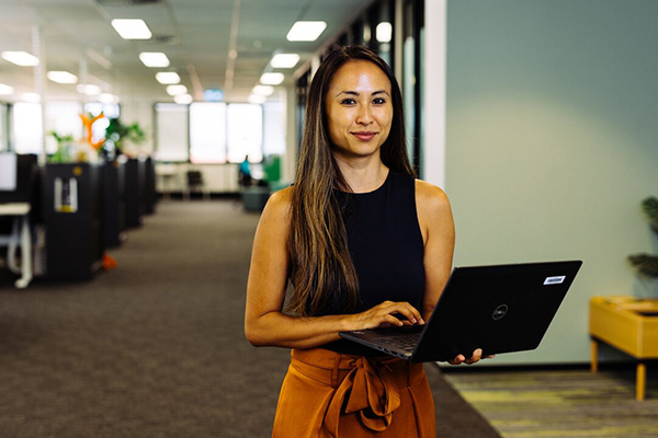 A woman in an office holds a laptop, focused on her work with a professional demeanor.