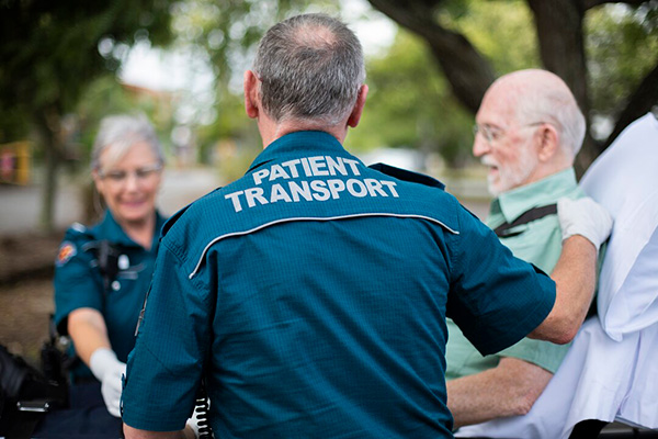 A man in a blue shirt and a woman in a green shirt engage in conversation with a man in a wheelchair.