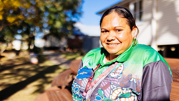 A woman wearing a green and blue shirt sits on a bench outdoors.