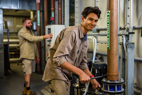 A man in a work uniform stands holding a pipe, ready for a plumbing task.