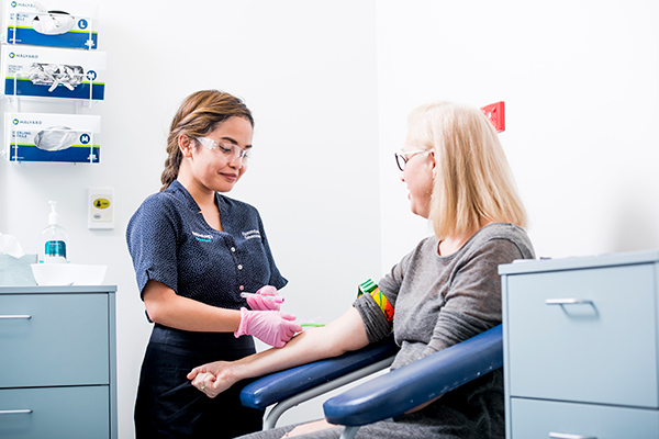 A woman is collecting blood from a woman's arm while she is sitting down.