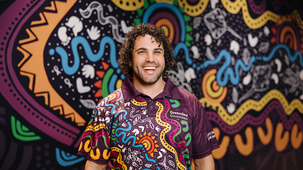 A man in a vibrant shirt stands against a brightly colored wall, showcasing a lively and artistic backdrop.