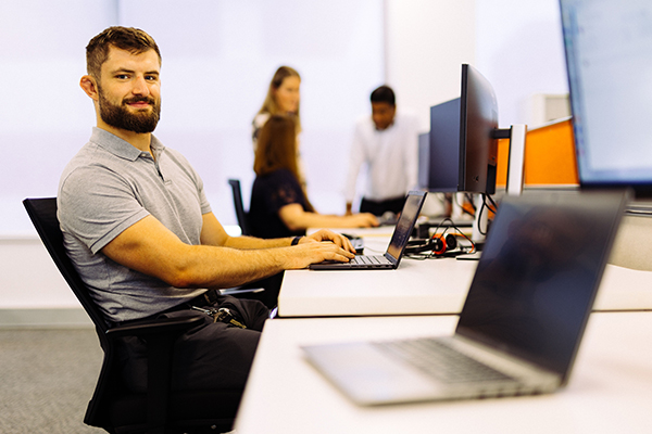 A man seated at a desk, focused on his work with a laptop.