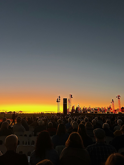 A diverse crowd of people gathered outdoors, admiring a vibrant sunset during an evening event.