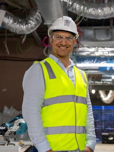 A smiling man wearing high vis workwear standing on a building site near electrical cables. 