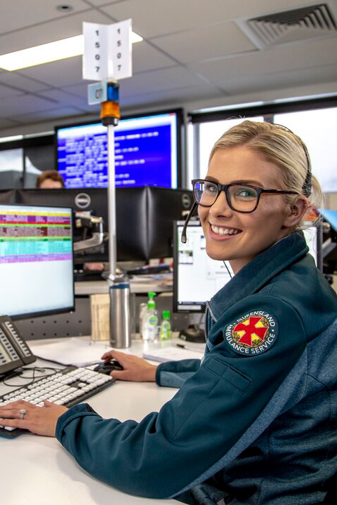A woman wearing a blue jacket and glasses sits at a desk, focused on her computer screen.