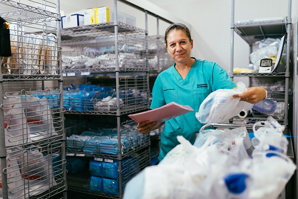 A woman in scrubs stands in a stock room with medical equipment.