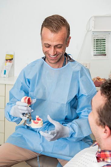 A dentist is showing a patient a model of a person's mouth and teeth.
