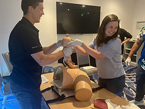 A man and woman collaborate on a dummy, adjusting its features and discussing their work intently.