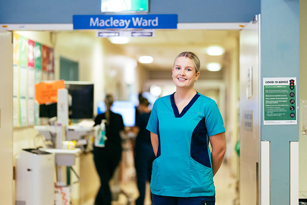 A nurse in scrubs stands in a hospital hallway.